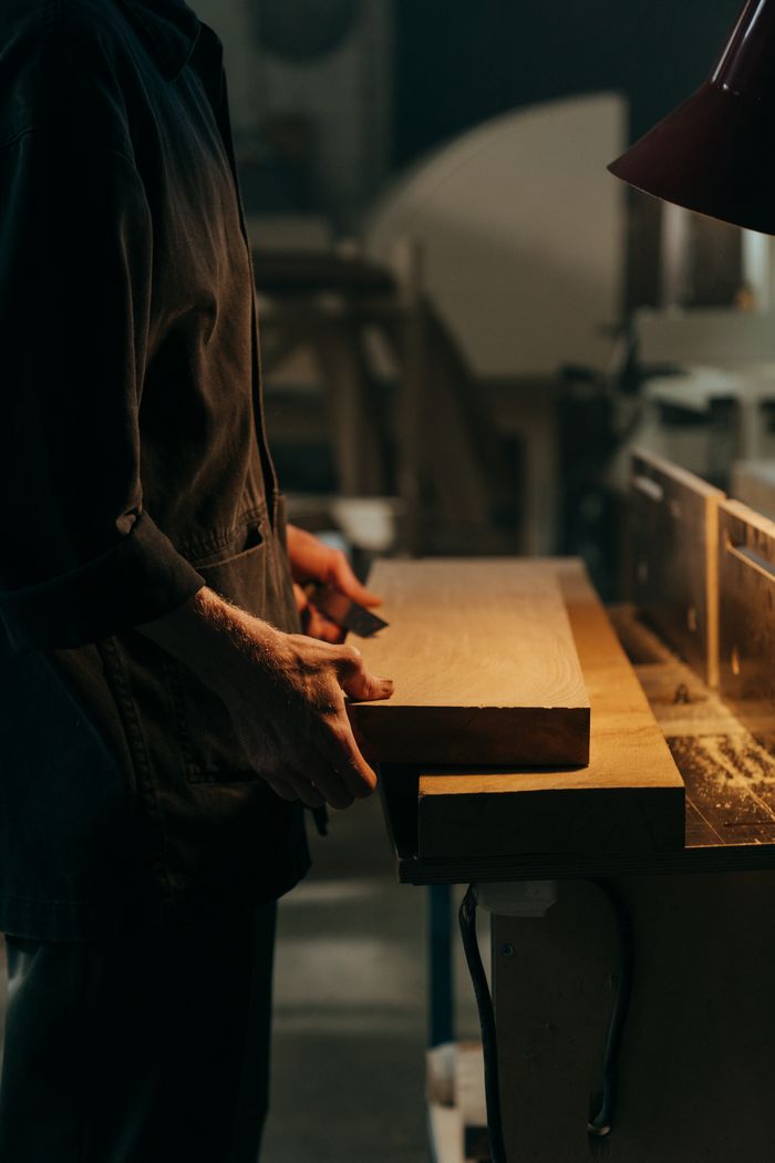 The Art of Drawing Readers In: Your attractive post title goes here A craftsman working with a wooden plank under focused lighting in a workshop.